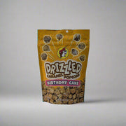 Two bags of Buc-ee’s Drizzled Caramel Popcorn, one in Black and White flavor and the other in Birthday Cake flavor, displayed on a white sheet backdrop.

