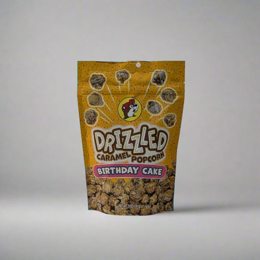 Two bags of Buc-ee’s Drizzled Caramel Popcorn, one in Black and White flavor and the other in Birthday Cake flavor, displayed on a white sheet backdrop.

