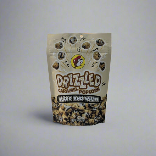 Two bags of Buc-ee’s Drizzled Caramel Popcorn, one in Black and White flavor and the other in Birthday Cake flavor, displayed on a white sheet backdrop.

