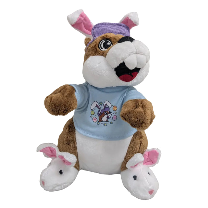 A brown and white plush beaver mascot sitting and wearing a purple hat with bunny ears, a light blue t-shirt with a Buc-ee bunny graphic, and white plush bunny slippers.