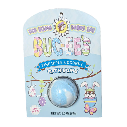 A Buc-ee's brand Pineapple Coconut bath bomb inside a clear plastic dome on a light blue, spring-themed cardboard backing. The packaging features a cartoon Buc-ee beaver in an egg, tree branches, and the text 'DID SOME BUNNY SAY BUC-EE’S' and 'PINEAPPLE COCONUT BATH BOMB'. Displayed on a clean white background.