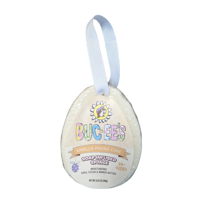 An egg-shaped soap-infused sponge in a cream-colored, spring-themed wrapper with a white ribbon loop for hanging. The label features a cartoon Buc-ee beaver in a daisy, with the text 'BUC-EE'S VANILLA POUND CAKE SOAP INFUSED SPONGE' and '30+ WASHES'. Displayed on a clean white background.