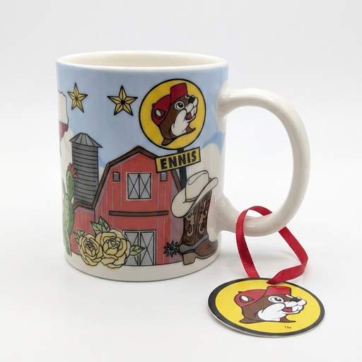 A small white ceramic Buc-ee's Ennis, TX mini mug featuring colorful Texas illustrations, including a red barn, yellow roses, cowboy boot with a hat, and a Buc-ee's sign reading "ENNIS". A red hanging ribbon with a circular Buc-ee's beaver logo tag is attached to the handle.