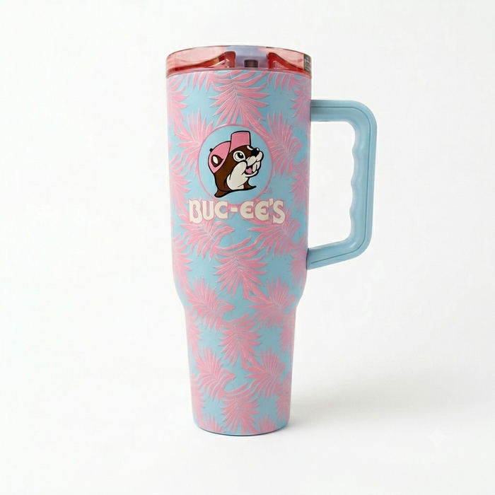 A 40-ounce Buc-ee's Fit Forty Pro travel tumbler with a light blue background and a pink palm leaf pattern. The front features the circular Buc-ee's beaver logo with the beaver wearing a pink cap above the word "Buc-ee's". The tumbler has a light blue ergonomic side handle and a translucent pink lid with a light blue flip-top cap. Displayed on a white background.