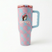 A 40-ounce Buc-ee's Fit Forty Pro travel tumbler with a light blue background and a pink palm leaf pattern. The front features the circular Buc-ee's beaver logo with the beaver wearing a pink cap above the word "Buc-ee's". The tumbler has a light blue ergonomic side handle and a translucent pink lid with a light blue flip-top cap. Displayed on a white background.