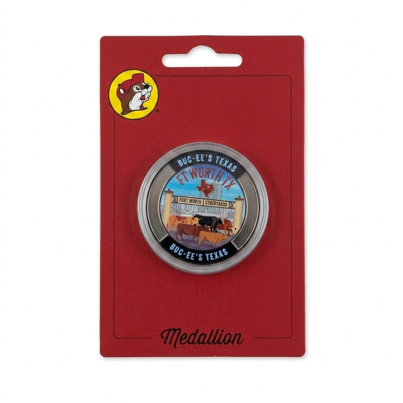 A circular metal souvenir medallion displayed inside a clear protective capsule on a red package card labeled "Medallion". The coin artwork includes the Fort Worth Stockyards gate, longhorn cattle, a red Texas shape, "FT WORTH TX" text, and a black rim stamped with "BUC-EE'S TEXAS".