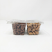 A side-profile product shot of a 4-compartment clear plastic tray filled with glazed nuts, shown against a seamless white background. This view highlights the depth of the containers, showing the generous portions of dark glazed pecans and golden glazed cashews through the transparent plastic walls. The flat, clear lid is securely fastened on top.