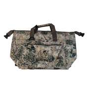 A front view of the Buc-ee's GameGuard 24 Can Cooler, a rectangular soft-sided cooler bag featuring a realistic Texas brush country camouflage print with prickly pear cactus details. The front pocket features an embroidered circular Buc-ee's beaver logo, and the top has brown webbed carrying handles with a padded grip wrap. Displayed on a white background.