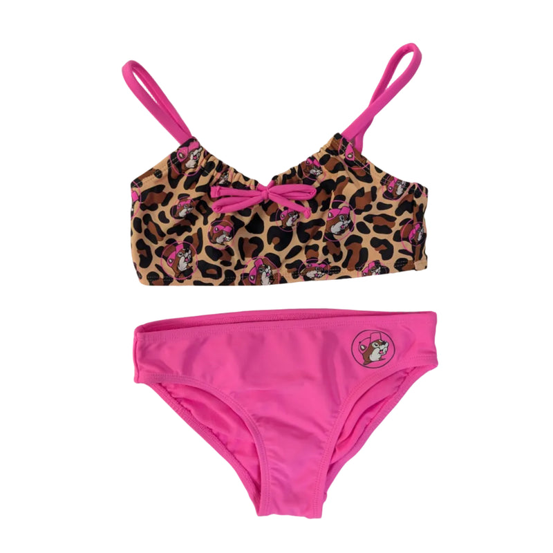 A girls' two-piece bikini set. The top features a leopard print pattern with pink Buc-ee's beaver icons and bright pink shoulder straps and pink bow in the middle of the chest. The matching bottoms feature a solid bright pink front with a small circular Buc-ee's mascot logo on the left hip, displayed on a clean white background.