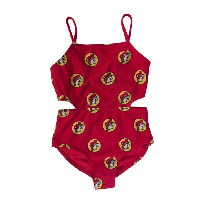 A flat lay product photograph of a Buc-ee's Red Logo one-piece girls' swimsuit featuring side cut-out details. The suit has thin camisole-style straps and a straight neckline. It is covered in an all-over repeating pattern of the yellow and red Buc-ee’s beaver logo. The garment is laid flat on a clean, white neutral surface.