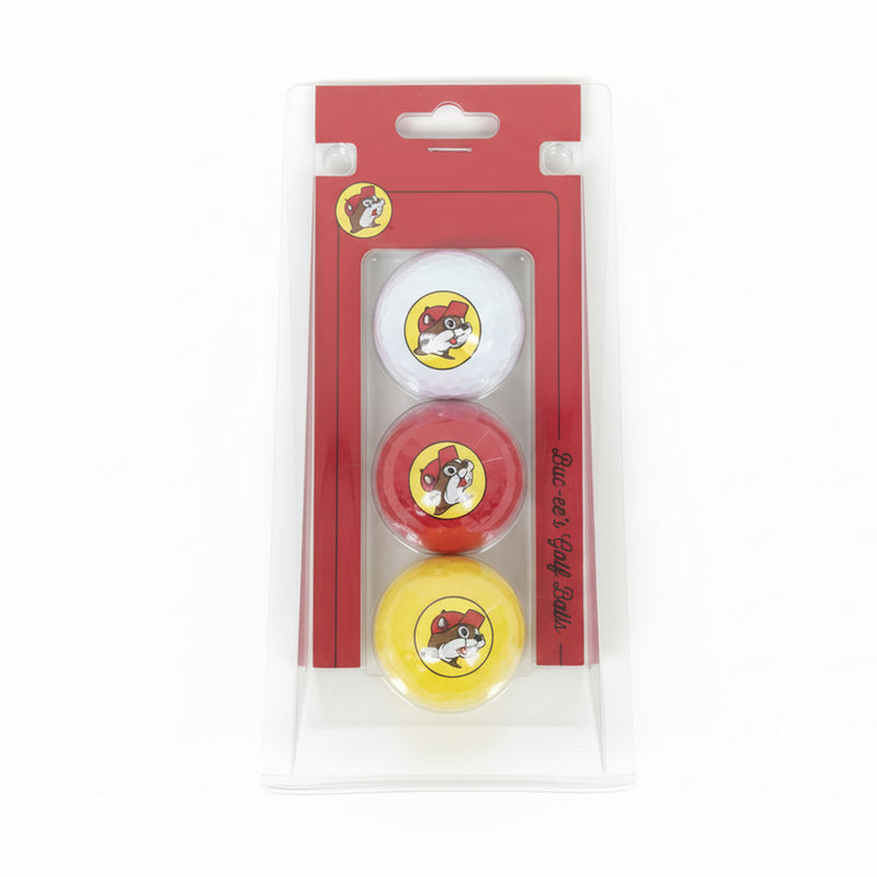 A photo of a Buc-ee’s 3-pack golf ball set in its original retail packaging. The set is displayed in a clear, transparent plastic blister pack with a red cardboard backing. Inside are three golf balls in vertical alignment: white on top, red in the middle, and yellow on the bottom, each featuring the full-color Buc-ee’s beaver logo. The red packaging includes the "Buc-ee’s Golf Balls" script on the side and a hanging slot at the top, shown against a clean, neutral white background.