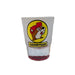 A front-facing product shot of a frosted Buc-ee's shot glass standing on a clean white surface. The front displays a circular yellow logo featuring the brown and white beaver mascot wearing a red cap, with a bold yellow and black box underneath reading "GOODYEAR" to commemorate the Arizona location. The shot glass features a thick, weighted base made of solid translucent red glass.