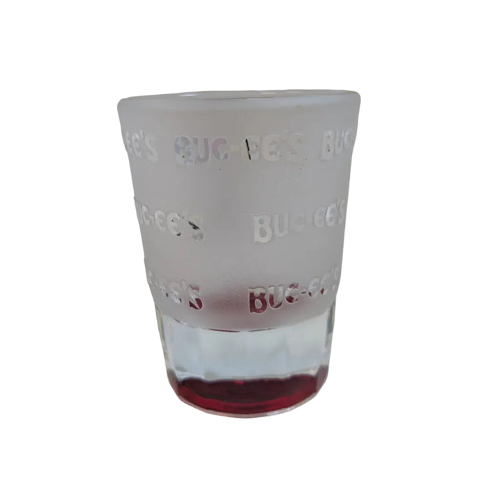 The rear view of the frosted Buc-ee's shot glass against a white background. This view highlights the semi-translucent, satin-frosted texture of the glass, embellished with a repeating pattern of clear, glossy "Buc-ee's" text wrapping around the body. The vibrant, solid red glass bottom is clearly visible at the base.