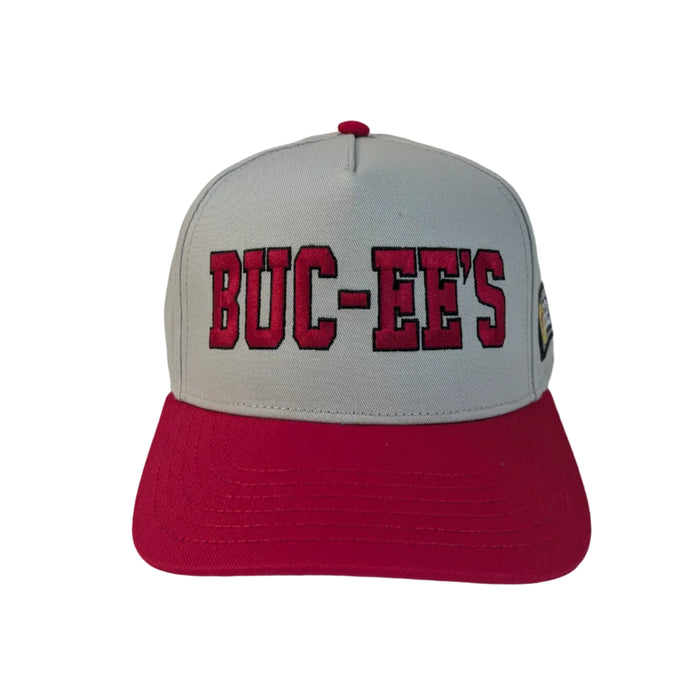 A product photo of a Buc-ee's Gray Hat with Red Embroidered Logo. A gray baseball cap with a vibrant red brim sitting on a white surface. The front of the cap features the text 'BUC-EE'S' embroidered in bold red letters. 