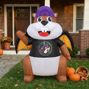 A 5.5-foot inflatable Buc-ee's beaver mascot wearing a purple cap, vampire t-shirt, and yellow bat wings displayed on a grassy front lawn in front of a home decorated with pumpkins and autumn flowers.