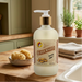 A close-up shot of a bottle of Beaver Nuggets hand soap standing on a wooden counter next to a white kitchen sink, with small potted plants and a folded towel in the background.