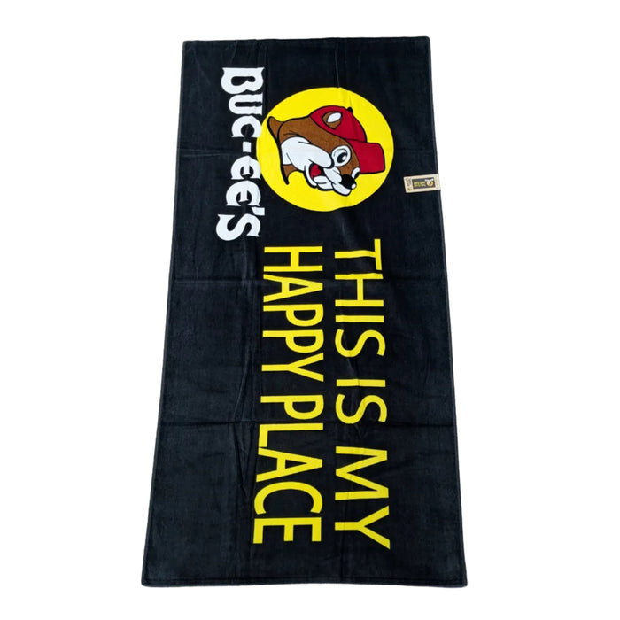A bold black beach towel featuring the Buc-ee's yellow sun logo at the top, followed by the words "THIS IS MY HAPPY PLACE" stacked in large, vibrant yellow block lettering. Displayed on a clean white background.