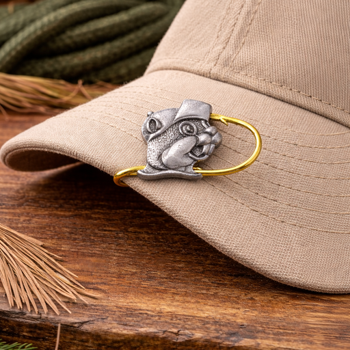 Buc-ee’s beaver hat hook clipped onto the brim of a beige baseball cap on a rustic wooden surface with an outdoor-style background.