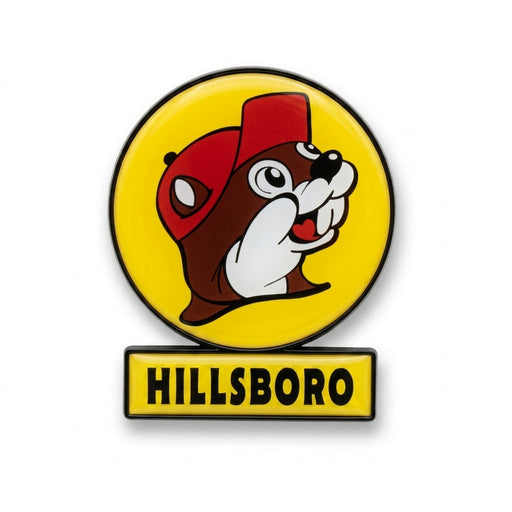 A circular yellow enamel magnet featuring the smiling Buc-ee's beaver wearing a red hat, with a small rectangular yellow sign attached directly below reading "HILLSBORO" in black text.