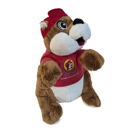 A 12-inch Buc-ee the Beaver plush toy sitting upright against a white background. The plushie has brown and white fur, a wide smile with two prominent front teeth, and large friendly eyes. He is wearing his signature red baseball cap and a small red t-shirt that displays the Buc-ee's logo and the words "HUBER HEIGHTS, OH" in white text.