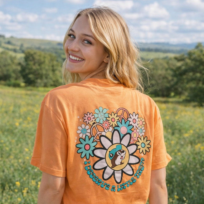 A woman standing in a field looking over her shoulder showing a back view of the Buc-ee's "I Deserve a Little Treat" Coral Shirt. 