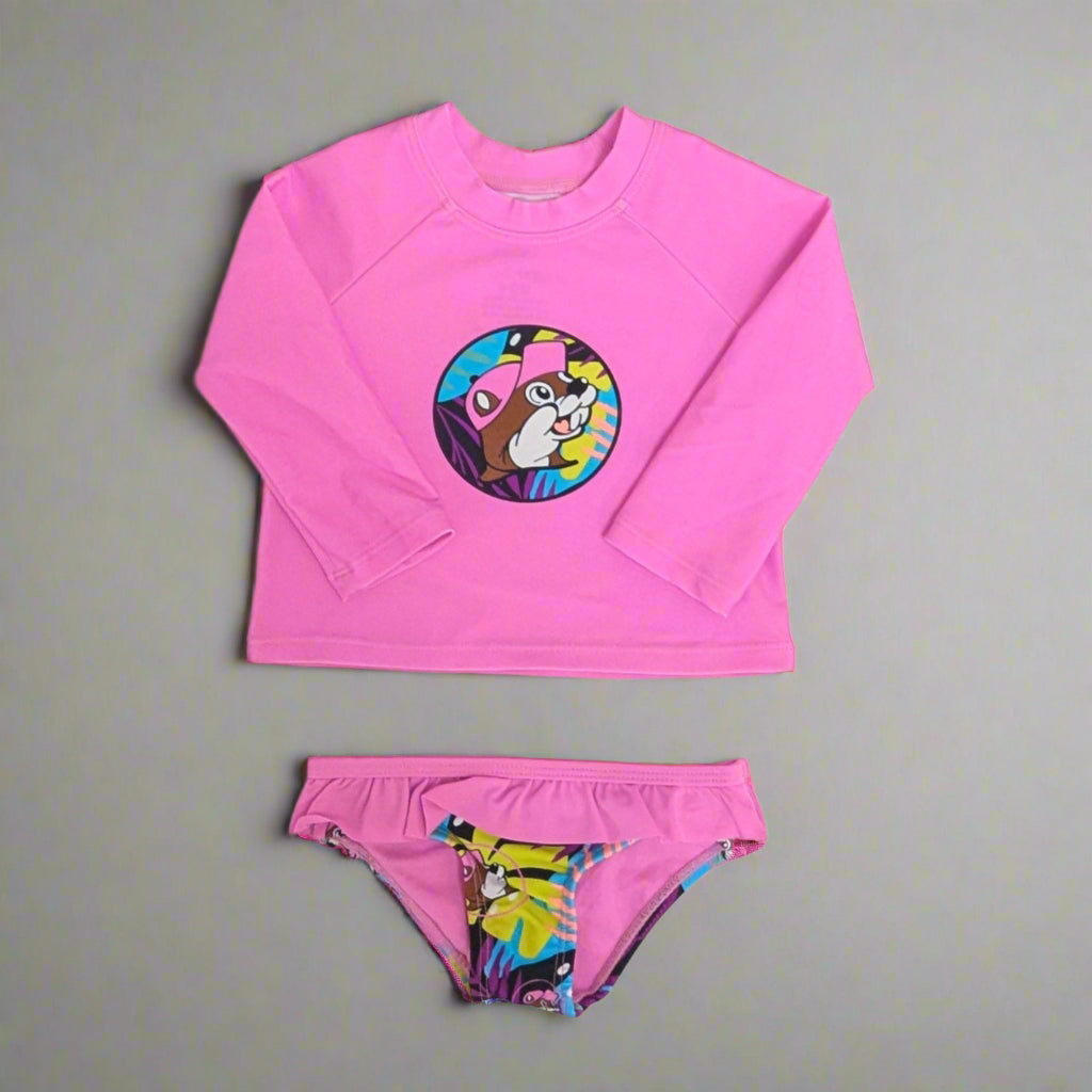 Buc-ee's Kids Tropical Swim Suit Set. Pink long sleeve top with logo on it and the bottoms have a tropcial design with ruffles. 