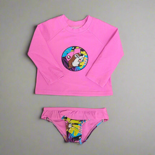 Buc-ee's Kids Tropical Swim Suit Set. Pink long sleeve top with logo on it and the bottoms have a tropcial design with ruffles. 