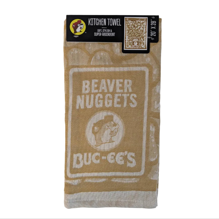 Buc-ee’s Beaver Nuggets kitchen towel in tan and white, featuring a large Beaver Nuggets snack bag design with the Buc-ee’s beaver logo and product branding. The 20" x 28" absorbent kitchen towel is displayed folded with its retail hanger and packaging attached against a white background.