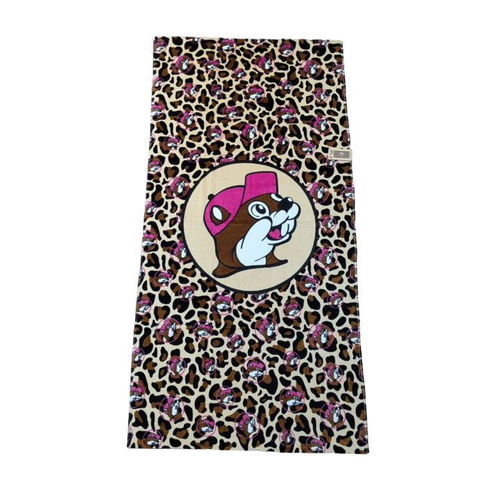 A trendy tan and black leopard print beach towel scattered with small pink Buc-ee’s logos. A large central emblem shows the beaver mascot wearing a bright pink cap. Displayed on a clean white background.