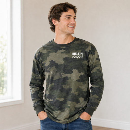 Man wearing a green camouflage Buc-ee’s long-sleeve shirt with a white Buc-ee’s logo and stars on the chest, paired with blue jeans in a bright indoor setting.