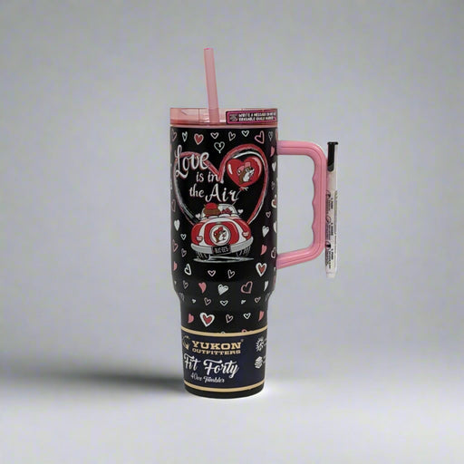 A black Valentine’s-themed tumbler featuring Buc-ee’s “Love is in the Air” design with hearts, a red car, and romantic details. The tumbler has a pink handle, reusable pink straw, and is crafted by Yukon Outfitters with a 40 oz capacity.
