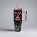 A black Valentine’s-themed tumbler featuring Buc-ee’s “Love is in the Air” design with hearts, a red car, and romantic details. The tumbler has a pink handle, reusable pink straw, and is crafted by Yukon Outfitters with a 40 oz capacity.