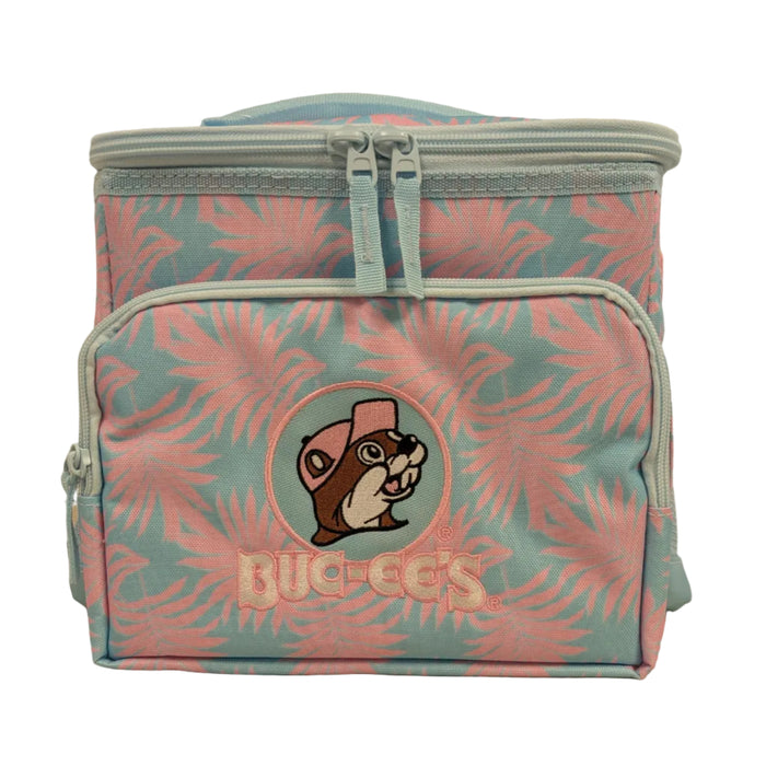 Front view of a rectangular Buc-ee’s insulated lunch box cooler featuring a blue and pink tropical palm leaf pattern. The front includes a zippered pocket with a large embroidered patch of the Buc-ee’s beaver logo in a pink hat, sitting above the "BUC-EE'S" name in pink lettering. The cooler has light blue zippers and a top carrying handle. Displayed on a clean white background.