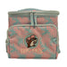 Front view of a rectangular Buc-ee’s insulated lunch box cooler featuring a blue and pink tropical palm leaf pattern. The front includes a zippered pocket with a large embroidered patch of the Buc-ee’s beaver logo in a pink hat, sitting above the "BUC-EE'S" name in pink lettering. The cooler has light blue zippers and a top carrying handle. Displayed on a clean white background.