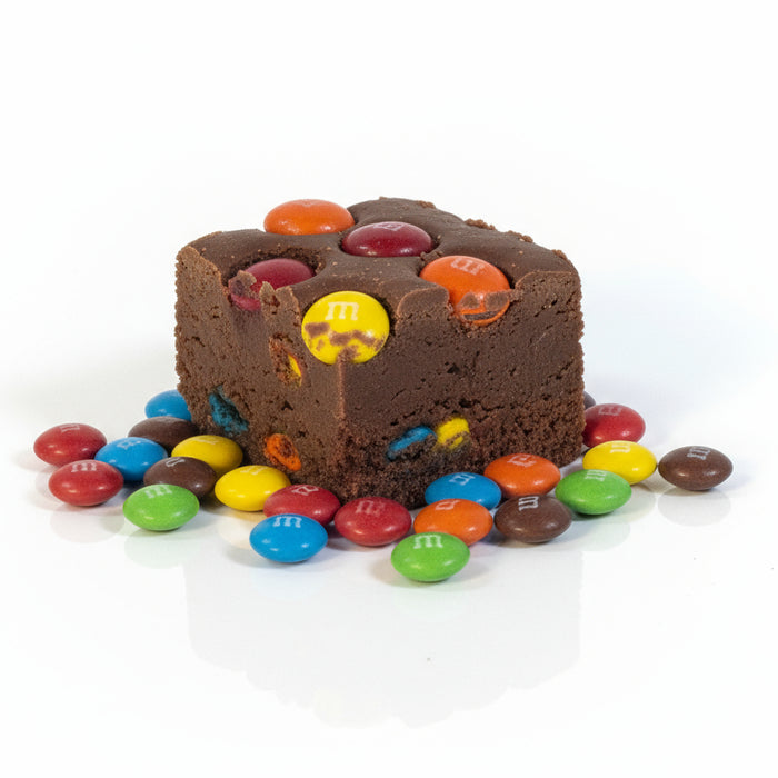 Small chocolate dessert with red and yellow toppings on a white background