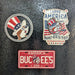 Three patriotic-themed pins on a textured black surface