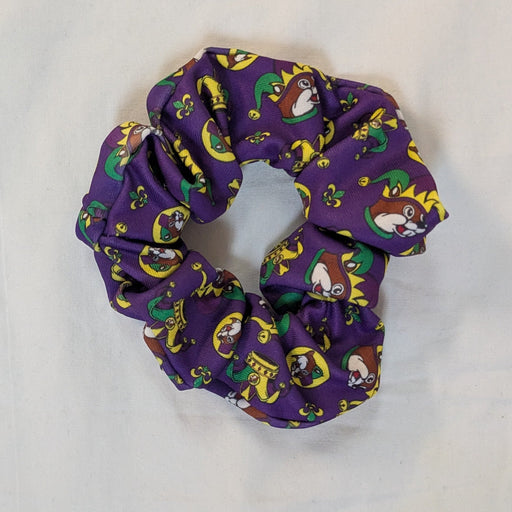 Purple Mardi Gras scrunchie featuring a repeating Buc-ee’s beaver mascot wearing jester hats, crowns, and masks in green, gold, and yellow, photographed flat on a white background.