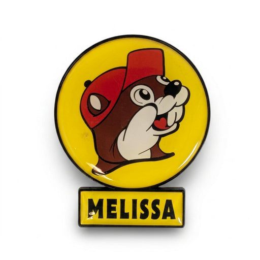 A circular yellow enamel magnet featuring the smiling Buc-ee's beaver wearing a red hat, with a small rectangular yellow sign attached directly below reading "MELISSA" in black text.