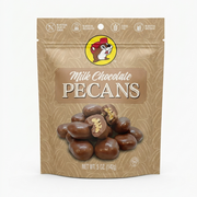 A professional product listing photo of a bag of Buc-ee's Milk Chocolate Pecans on a clean white background. The beige stand-up pouch features the iconic Buc-ee's beaver logo at the top center. Text below reads 'Milk Chocolate PECANS' above a pile of chocolate-covered pecans, two of which are cut in half. Dietary claims are at the top, and 'NET WT. 5 OZ. (142g)' is at the bottom. The lighting is bright and even.
