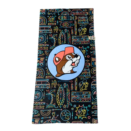 A black beach towel featuring a vibrant "Tiki Neon" pattern with colorful, stylized surfboards, tribal suns, and the Buc-ee's logo in neon blue, orange, and yellow. Displayed on a clean white background.