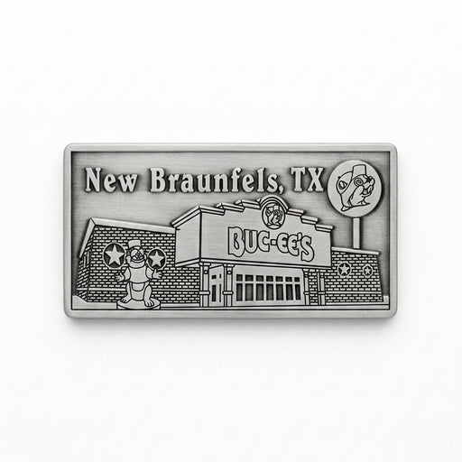 A rectangular pewter metal magnet showing an embossed 3D relief of the Buc-ee's New Braunfels travel center building, complete with the beaver statue out front, the Buc-ee's sign, a lollipop road sign in the upper right, and the word "New Braunfels" in the upper left corner.
