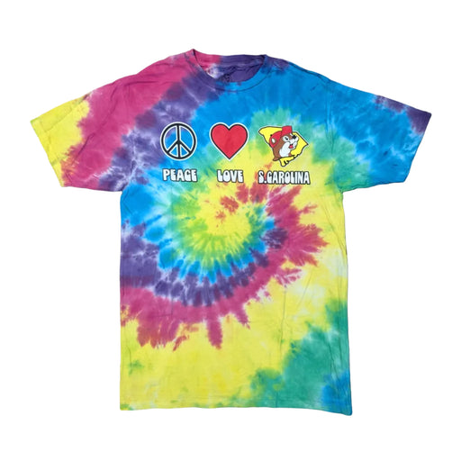 A short-sleeve crew neck t-shirt featuring a vibrant multi-colored spiral tie-dye pattern with swirls of pink, purple, blue, yellow, and green, laid flat against a white background. Across the chest are three distinct icons side-by-side: a blue peace symbol, a red heart, and a yellow silhouette map of South Carolina containing the Buc-ee's beaver mascot wearing a red baseball cap. Below the symbols, the words "PEACE", "LOVE", and "S.CAROLINA" are printed in a bold white font.