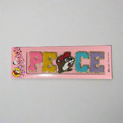 Two Buc-ee’s sticker patches shown on pink packaging: one spells “LOVE” with Buc-ee’s face as the “O,” and the other spells “PEACE” with Buc-ee in the center, both in colorful glitter letters.


