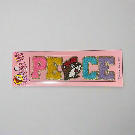Two Buc-ee’s sticker patches shown on pink packaging: one spells “LOVE” with Buc-ee’s face as the “O,” and the other spells “PEACE” with Buc-ee in the center, both in colorful glitter letters.

