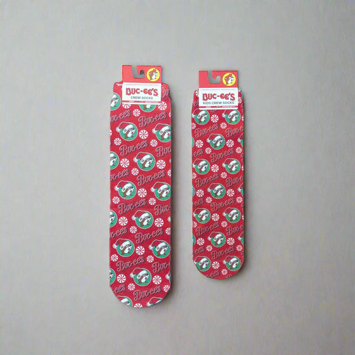Two pairs of Buc-ee’s Peppermint Christmas Crew Socks, one kids’ size and one adult size, featuring a red background with candy canes, peppermints, and Buc-ee’s logos.