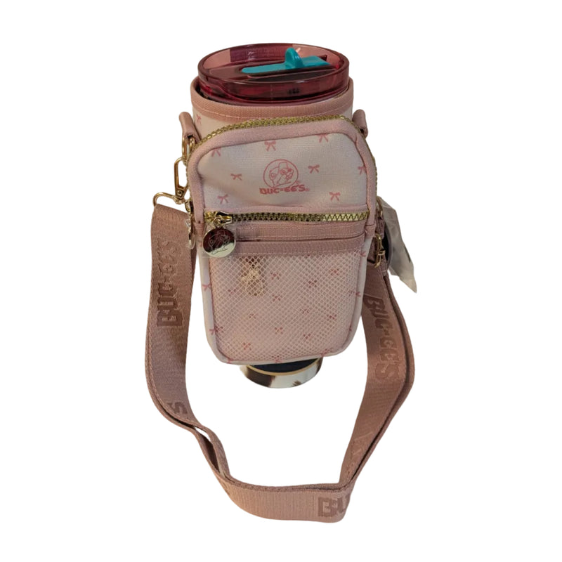 A photo of a tumbler inside a Buc-ee's pink crossbody tumbler bag that features a pink Buc-ee's logo printed on the front zippered pocket, gold hardware, and an adjustable shoulder strap.