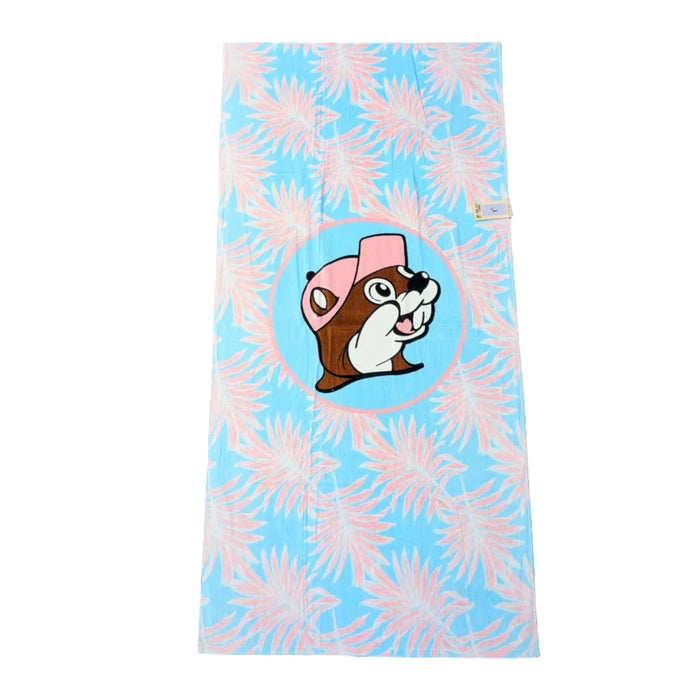 A summery beach towel featuring a pattern of soft pink and light blue palm fronds. Centered is the Buc-ee's beaver mascot wearing a pink hat within a pink circular border. Displayed on a clean white background.