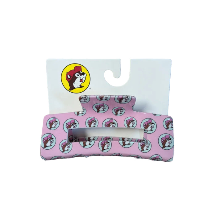 A medium-sized pink hair claw clip displayed on a white branded backing card. The clip is covered in a repeating pattern of the Buc-ee's beaver mascot inside small light-blue circles. The beaver is wearing a pink hat to match the clip's base color. The top left of the backing card features the classic yellow and red Buc-ee's logo.