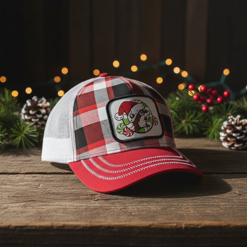 The front has a plaid design with the Buc-ee's logo in a santa hat with green and red peppermint candies. The bill of the hat is red with white stitching and the back is a mesh white trucker style. 