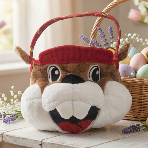Plush beaver-shaped Easter basket with a red hat on a wooden table, surrounded by Easter eggs and flowers.